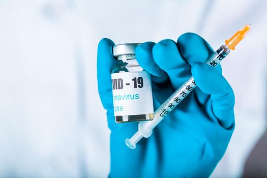 Woman doctor or nurse in uniform and gloves wearing face mask protective in lab holding medicine vial vaccine bottle with COVID-19 Coronovirus vaccine label