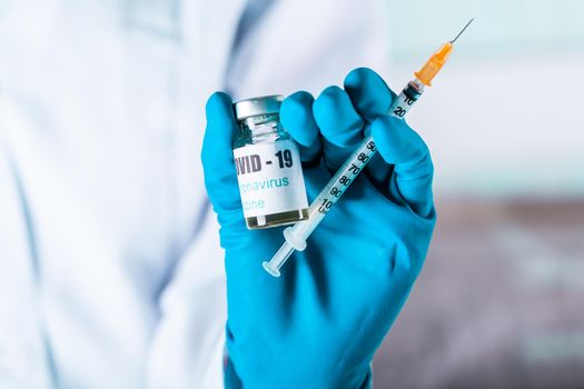 Woman doctor or nurse in uniform and gloves wearing face mask protective in lab holding medicine vial vaccine bottle with COVID-19 Coronovirus vaccine label