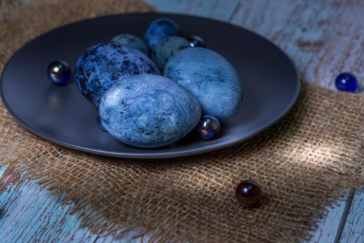 Blue Easter eggs on a dark ceramic plate on burlap on an light wooden background.Spring religious holidays.