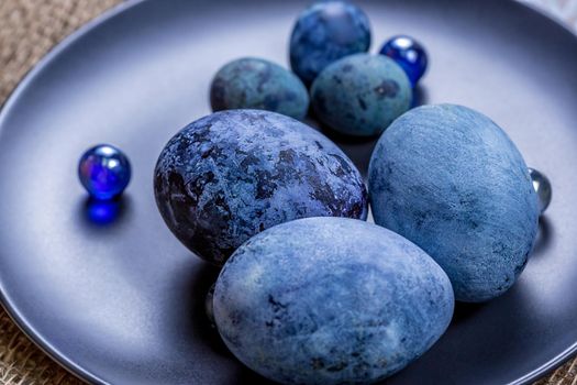 Blue Easter eggs on a dark ceramic plate on burlap on an light wooden background.Spring religious holidays.