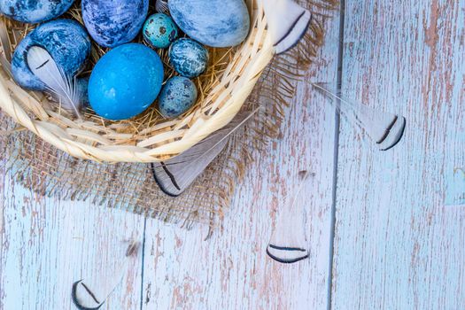 Easter eggs painted with natural dye in a rustic, natural style. Eggs in a nest of hay in a wicker basket on burlap on an light wooden background. Copy space.