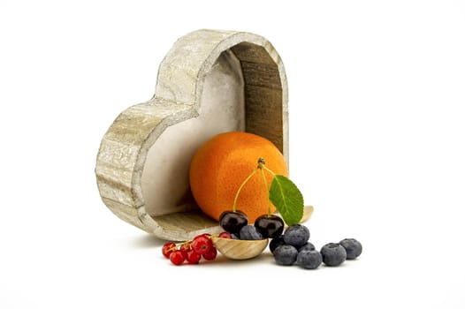 Culinary still life with orange, wooden spoons, cherries and orange, red currants and blueberries over an off white background with copy space