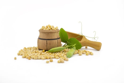 Dried peas spilling from a wooden barrel, wooden scoop and fresh plant with pods isolated on a white background