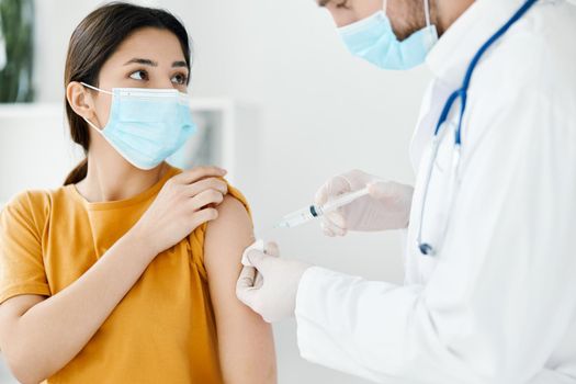 side view of doctor injecting vaccine into shoulder of patient wearing medical mask in hospital epidemic. High quality photo