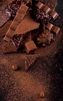 Broken chocolate pieces and cocoa powder on wooden background