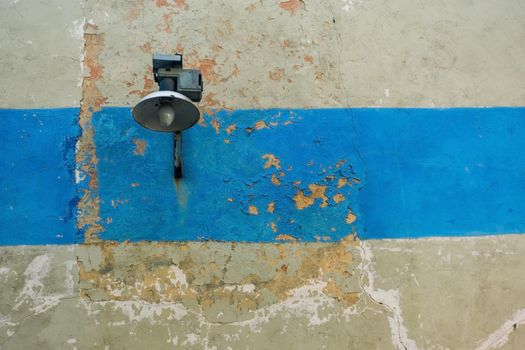 Street lamp on the wall with a crack and a blue stripe. An old wall with a street lamp. Textured wall with a lantern.