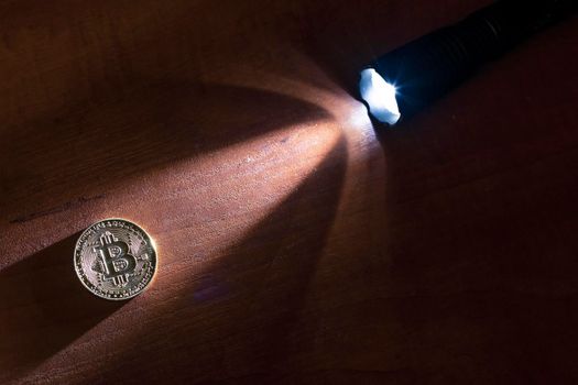 Bitcoin coin lit by a ray of light from a flashlight.