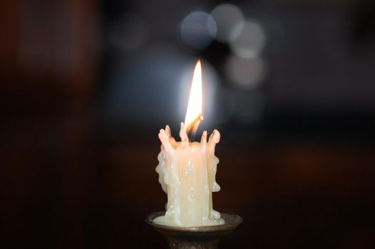 The candle burns on a dark background.  Frozen fosk on a candle that burns. White candle on a candlestick in the center.