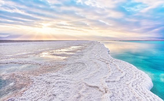 Morning sun shines on salt crystals formations, clear cyan green calm water near, typical landscape at Ein Bokek beach, Israel.