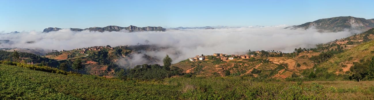 Fog over valley with small village on sunny morning in region near Alakamisy Ambohimaha, Madagascar.