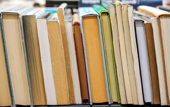 Row of many old used books displayed at local antiquarian bookshop, shallow depth of field photo, only few pages in focus.