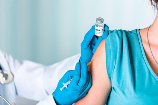Woman doctor or nurse in uniform and gloves wearing face mask protective in lab, making an injecion holding vaccine bottle with COVID-19 Coronovirus vaccine label