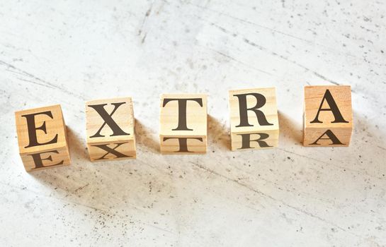 Five wooden cubes with word EXTRA on white stone like board, view from above.