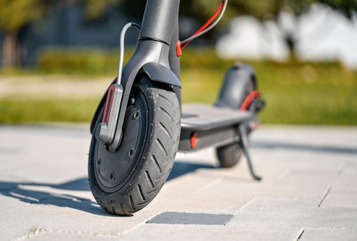 Electric scooter parked on tiled stone pavement - closeup detail on front wheel.