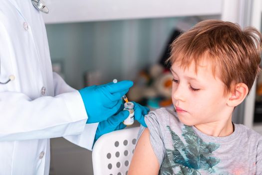 Woman doctor or nurse in uniform and gloves wearing face mask protective in lab, making an injecion to a kid holding vaccine bottle with COVID-19 Coronovirus vaccine label