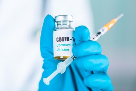 Woman doctor or nurse in uniform and gloves wearing face mask protective in lab, holding medicine vial vaccine bottle with COVID-19 Coronovirus vaccine label