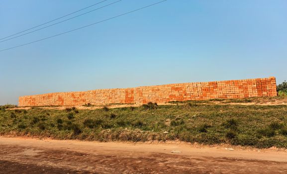 Orange red bricks made from local clay arranged in wide stack, ready for building a house near the road.