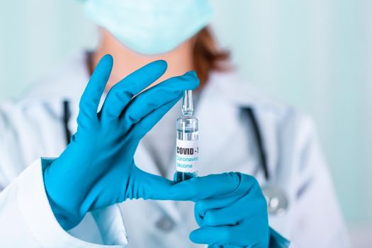 Woman doctor or nurse in uniform and gloves wearing face mask protective in lab, holding medicine vial vaccine bottle with COVID-19 Coronovirus vaccine label