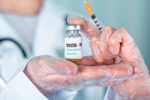 Woman doctor or nurse in uniform and gloves wearing face mask protective in lab, holding medicine vial vaccine bottle with COVID-19 Coronovirus vaccine label