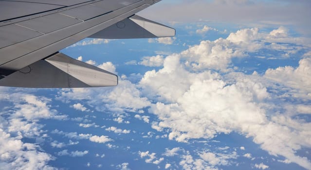 View from passenger window of commercial airplane, clouds on blue sky visible under aircraft wing.