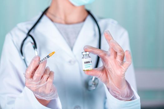 Woman doctor or nurse in uniform and gloves wearing face mask protective in lab, holding medicine vial vaccine bottle with COVID-19 Coronovirus vaccine label