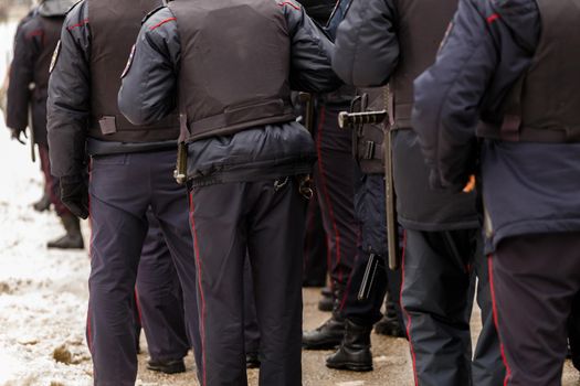 Tula, Russia - January 23, 2021: Crowd of police officers in black uniform with bulletproof vests and pistols - view from back. Close-up.