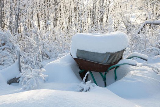 Snow wheelbarrow with construction debris under a pile of snow, side view.