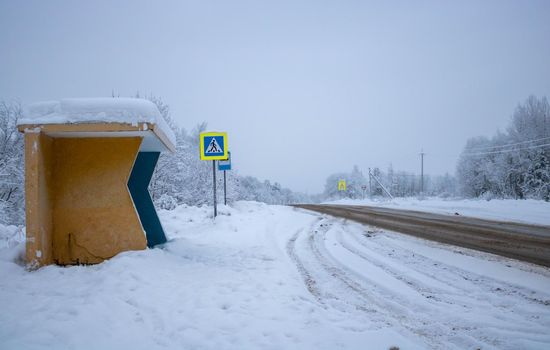 Country highway with an interchange, car tracks in a dirt snow close-up. Forest road on a cloudy winter day. A view from a bus stop. Transportation, dangerous driving, winter tires, remote places