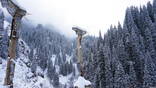 An old abandoned gazebo with views of the snowy mountains and forest. Clouds float beautifully, fir trees are covered with snow. High white hills. The stone pillars of the building are destroyed.