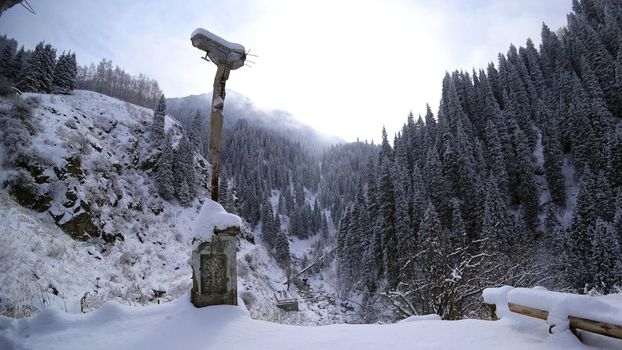 An old abandoned gazebo with views of the snowy mountains and forest. Clouds float beautifully, fir trees are covered with snow. High white hills. The stone pillars of the building are destroyed.