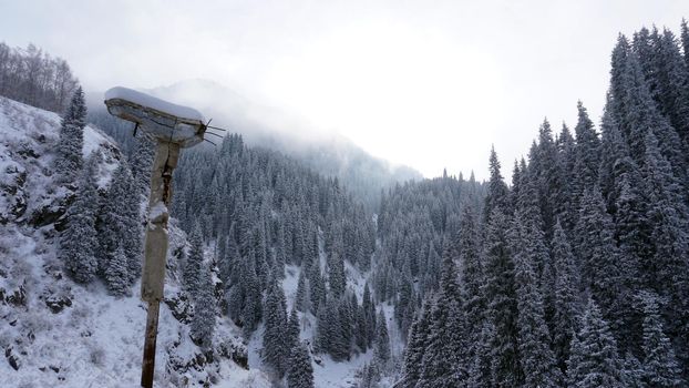 An old abandoned gazebo with views of the snowy mountains and forest. Clouds float beautifully, fir trees are covered with snow. High white hills. The stone pillars of the building are destroyed.