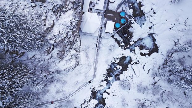 Hot springs in the snowy forest and mountains. Top view from the drone on the white gorge with the river. There are barrels of radon water. There is steam, people are bathing. Almarasan, Almaty.