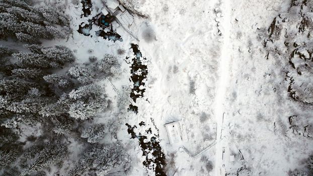 Hot springs in the snowy forest and mountains. Top view from the drone on the white gorge with the river. There are barrels of radon water. There is steam, people are bathing. Almarasan, Almaty.