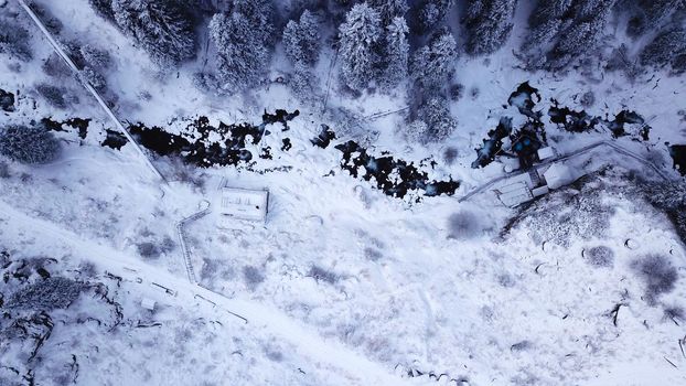 Hot springs in the snowy forest and mountains. Top view from the drone on the white gorge with the river. There are barrels of radon water. There is steam, people are bathing. Almarasan, Almaty.