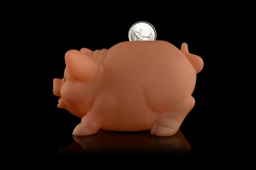 An isolated over a black background image of a piggy bank profile shot with a coin being inserted.