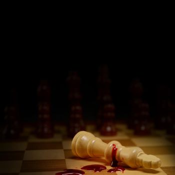 A Chessboard game in the position of checkmate spotlighting the dead King laying in a pool of blood.
