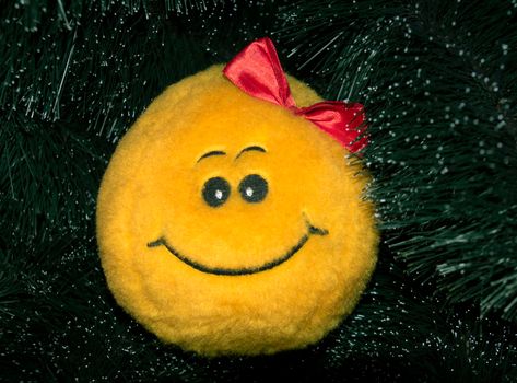 Smiley yellow soft toy with a bow on the Christmas tree.