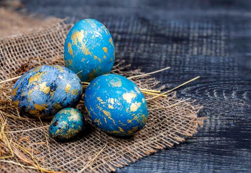 Easter decoration concept: blue painted eggs on the sackcloth with hay close-up on dark background. Spring religious holidays.