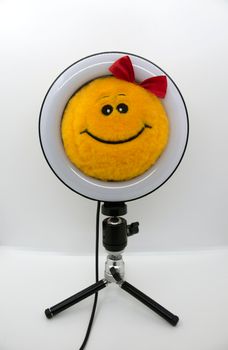 Smiley yellow soft toy with a red bow in a ring lamp.