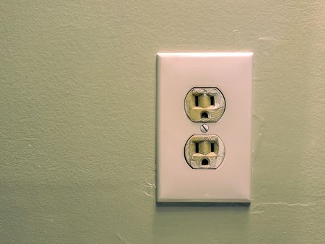 White electrical wall outlet with two sockets mounted on a green painted wall.