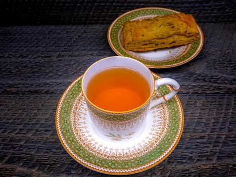 Hot tea in vintage picture of antique hot tea cup and bakery in saucer on wood background
 Hot tea in vintage picture of antique hot tea cup and bakery in saucer on wood background