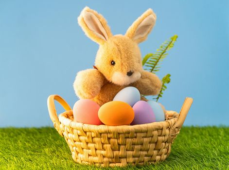 Easter bunny toy and Easter eggs in basket on green grass