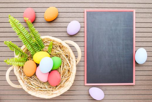 Colorful easter eggs in the basket and blackboard on wood background with space