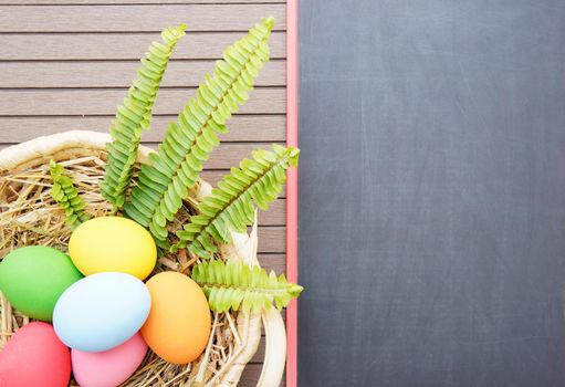 Colorful easter eggs in the basket and blackboard on wood background with space