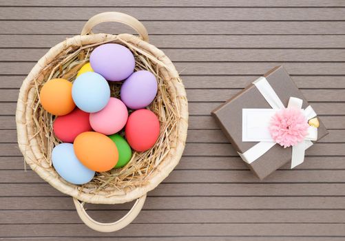 Colorful easter eggs in the basket and gift box on wood background with space