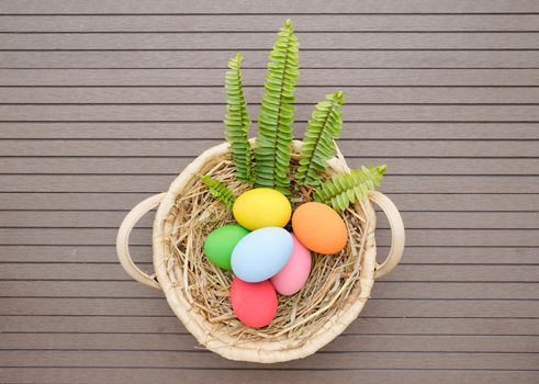 Colorful easter eggs in the basket on wood background with space