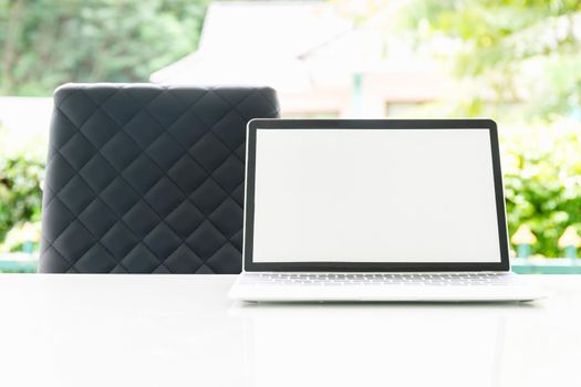 Laptop computer and cup of coffee on the table outdoor in morning with blurred green plant background