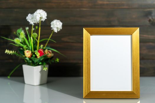 Picture mock up with golden frame and Artificial flower vase bouquet over table with wood wall background