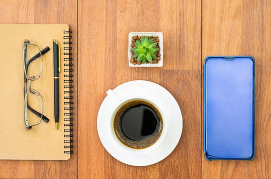 Top view image of coffee cup ,notebook and cellphone with eye glasse on wooden table background for adding text or mockup