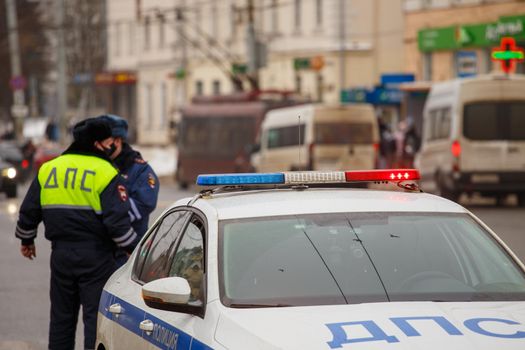 Tula, Russia - January 23, 2021: Russian road police officers standing near patrol car and dirty snow on winter city road - close-up with selective focus on roof lamp. Letters DPS mean Traffic Patrol Police